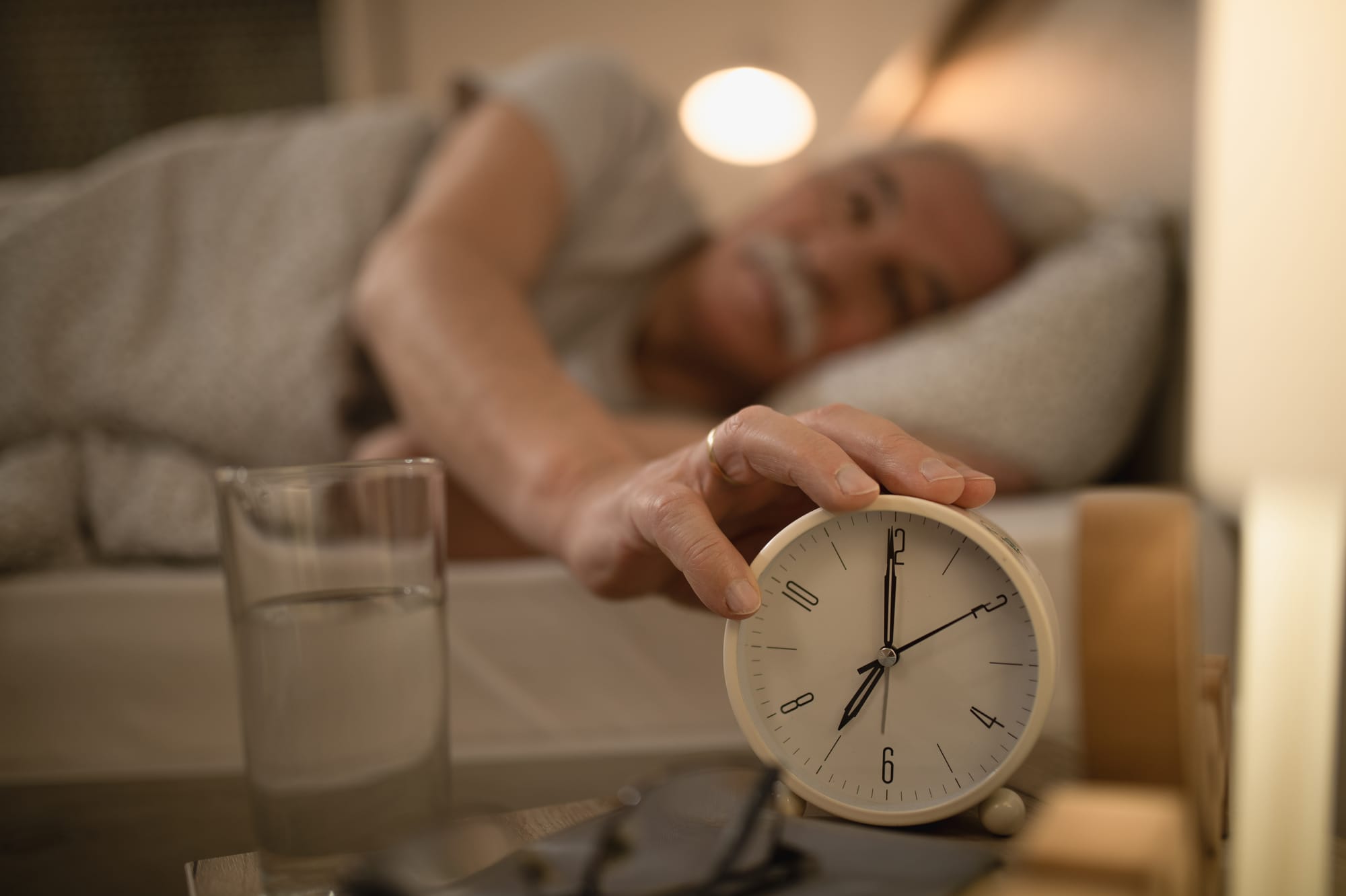 An older man sleeping and touching his alarm clock